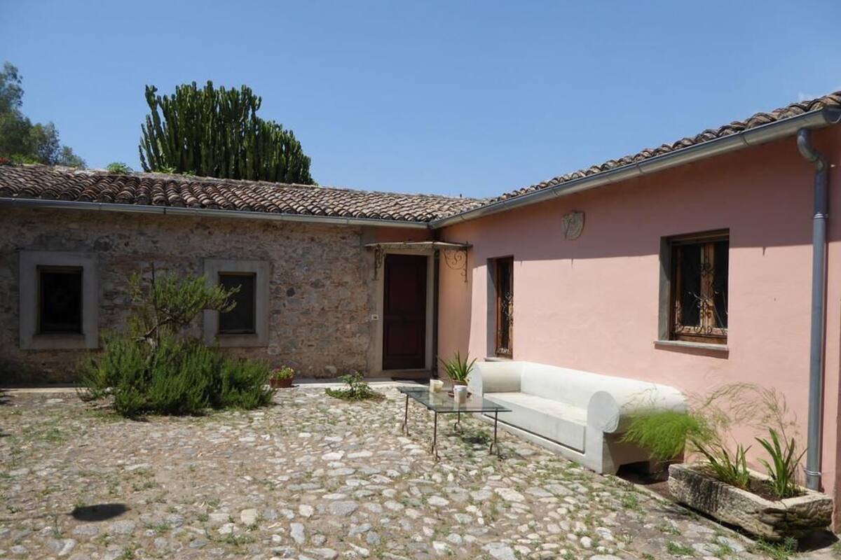 Un bâtiment en pierre avec un toit recouvert de tuiles, un canapé blanc pour l’extérieur et une petite table sur laquelle est posée une plante.