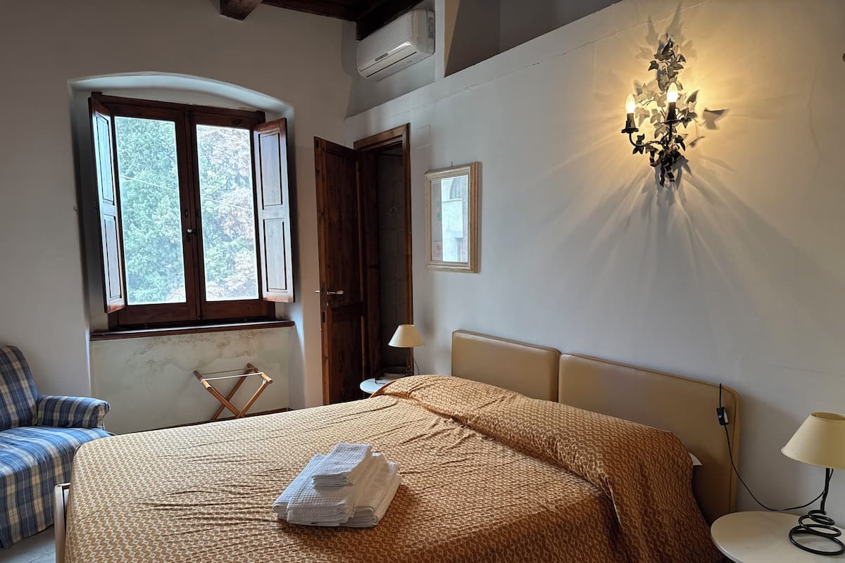 Une chambre à coucher avec un lit, une chaise, une lampe et une fenêtre avec des volets.