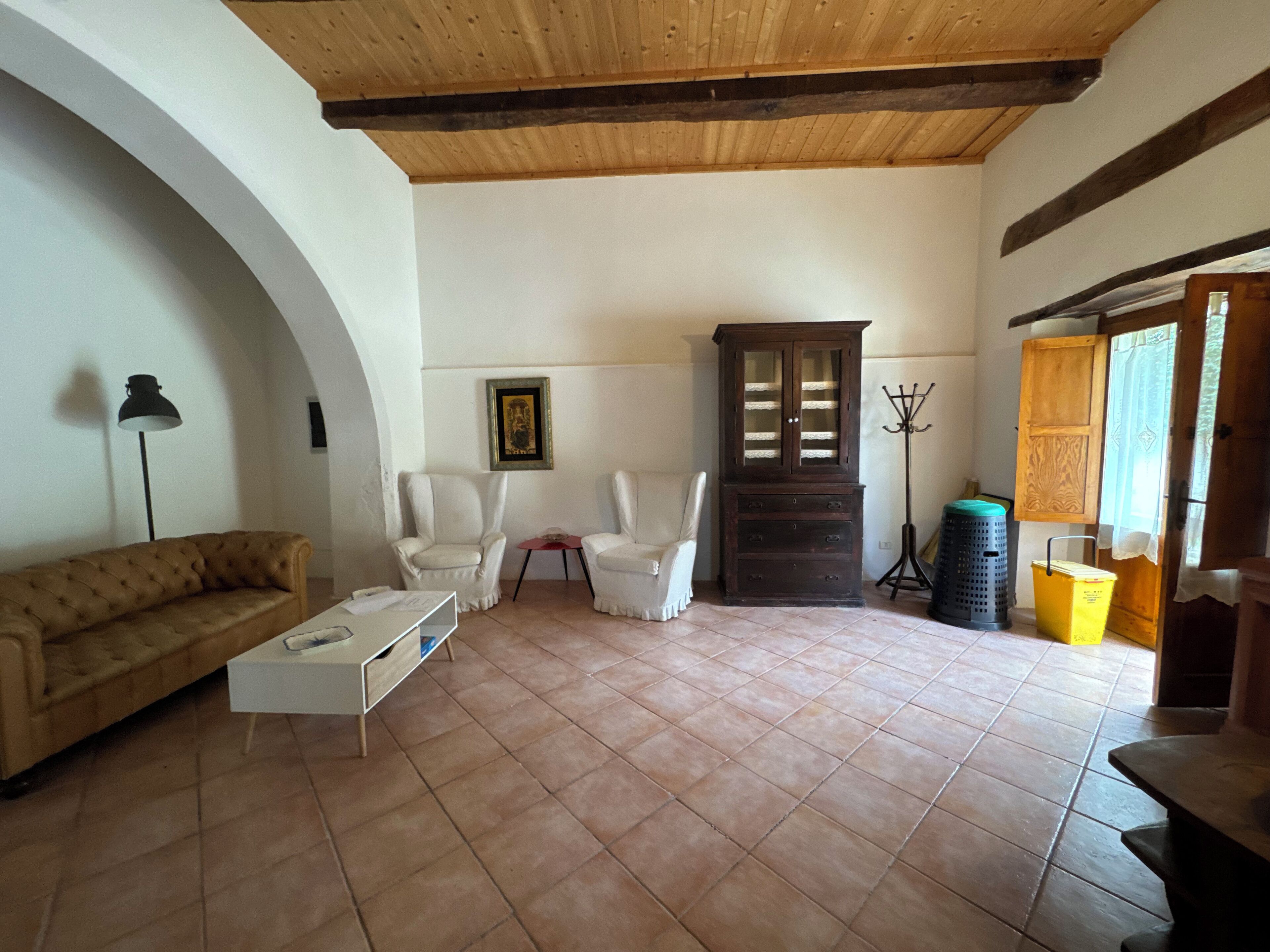 A living room with a wooden ceiling, a sofa, two armchairs, a cabinet, and a tiled floor.
