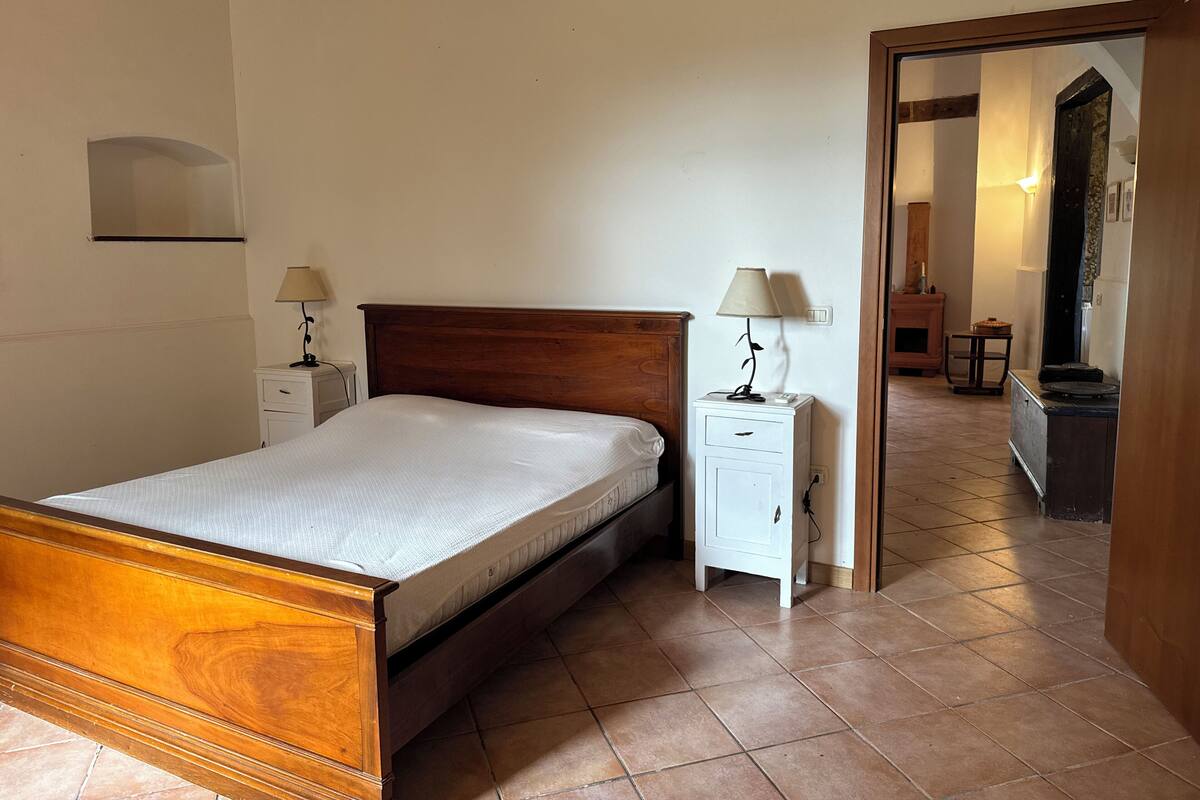 Une chambre à coucher avec un lit en bois, deux tables de chevet avec des lampes, une armoire blanche et un sol carrelé.