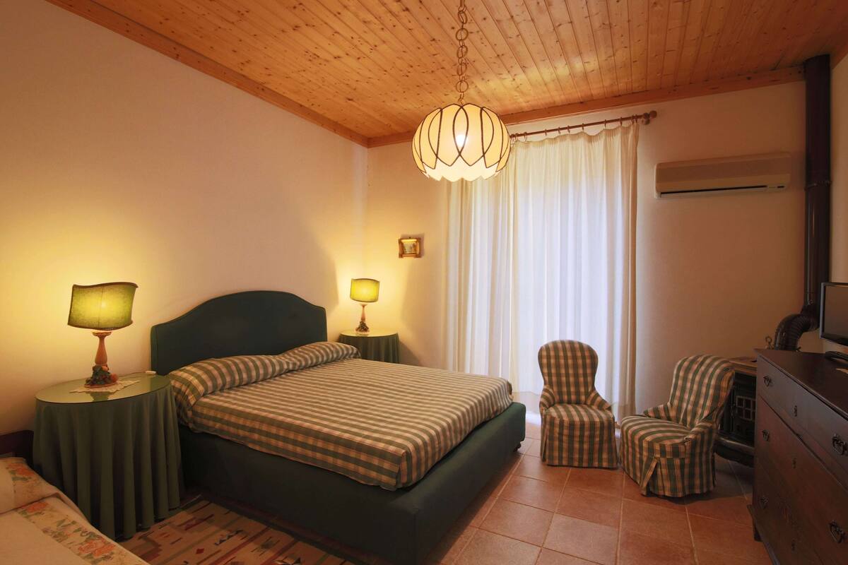 Une chambre à coucher avec un lit, deux tables de chevet avec des lampes, une chaise, une commode et une fenêtre avec des rideaux.