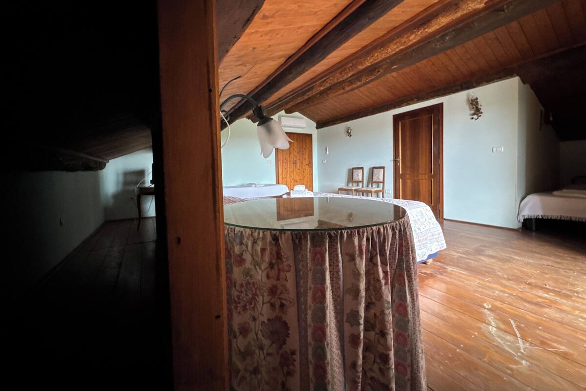 Une pièce avec un plafond en bois, un lit recouvert d’une couvre-lit à motifs floraux et une petite table recouverte d’une nappe blanche.