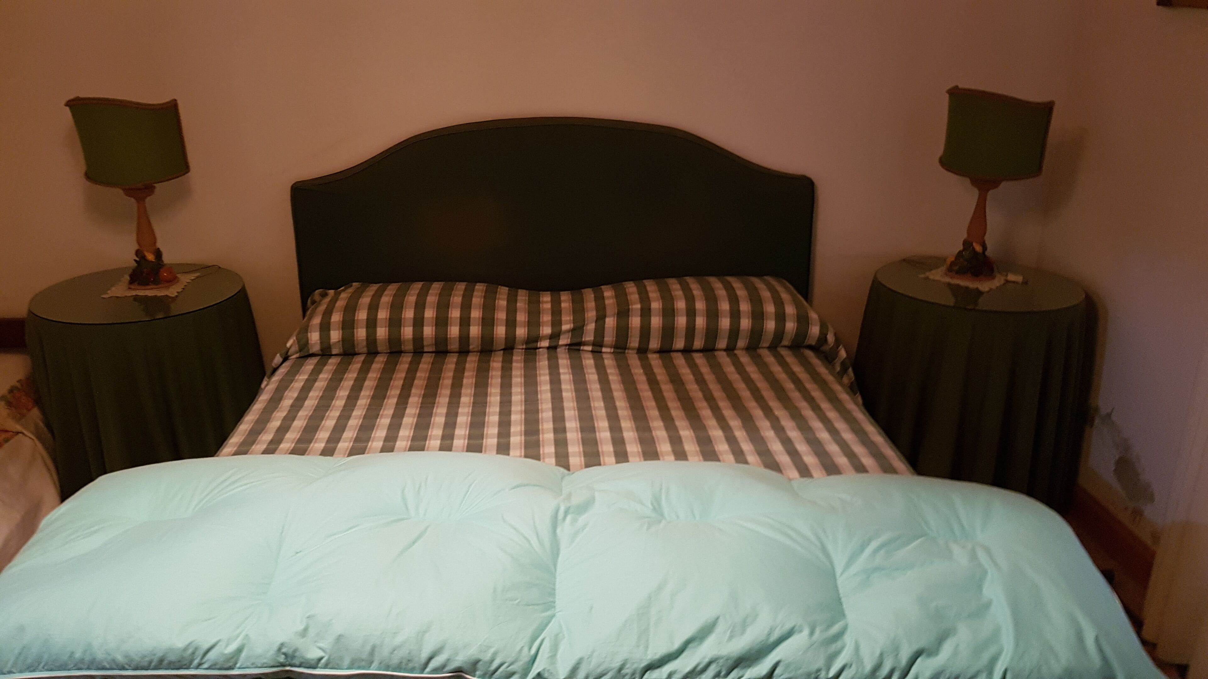 Un lit avec une couvre-lit à carreaux et une couette bleu clair. Il y a deux tables de chevet, chacune avec une lampe, de chaque côté du lit.