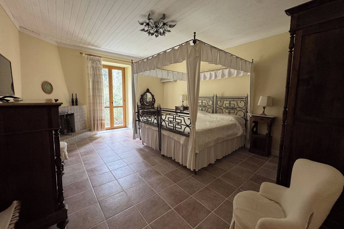 Une chambre à coucher avec un lit à baldaquin, une commode en bois, une chaise et une cheminée.