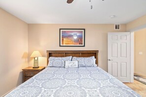 Ein Schlafzimmer mit Bett, Nachttisch mit Lampe, gerahmtem Bild an der Wand und einer Tür.