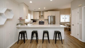 Una cocina moderna con armarios blancos, un refrigerador de acero inoxidable, un microondas y una estufa a gas. Hay tres taburetes negros en la isla.