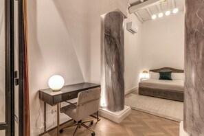 Ein modernes Schlafzimmer mit Schreibtisch, einer großen Marmorsäule, einem Bett und einem Nachttisch mit Lampe.