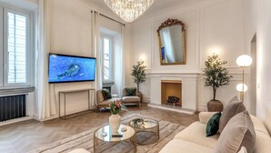 A spacious living room with a fireplace, comfortable seating, a television, and decorative plants.