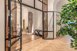 Ein modernes Interieur mit Fischgrätparkett, Glastüren und einer großen Pflanze.