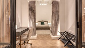 A modern bedroom with a bed, desk, and chair, featuring marble columns and a herringbone floor.
