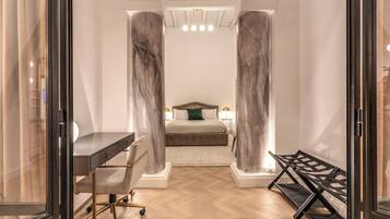 A modern bedroom with a bed, desk, and chair, featuring marble columns and a herringbone floor.
