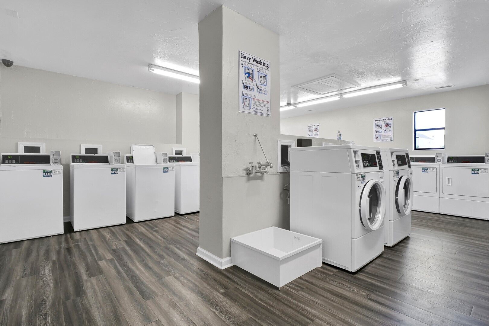 A laundry facility with multiple washing machines and dryers, wooden flooring, and instructional posters on the walls.