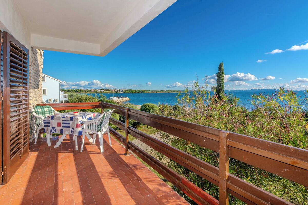 Ein Balkon mit Tisch und Stühlen, der auf ein Gewässer und eine ferne Küste blickt.