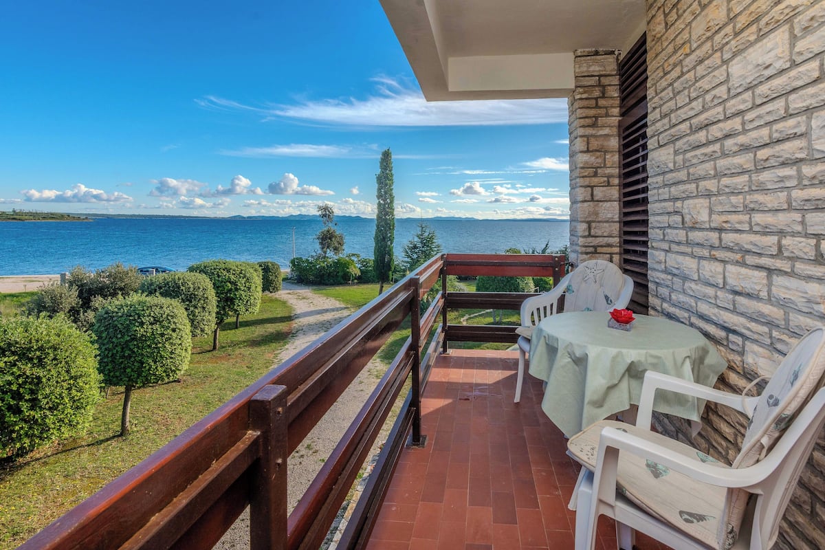 Ein Balkon mit Seeblick, einem Tisch mit Stühlen und einer Steinmauer.