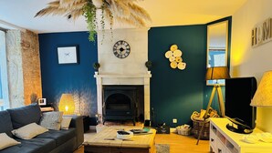 A cozy living room with a fireplace, a sofa, a coffee table, and a TV. - Le "33" Gîte de Charme coeur Cotentin (Valognes)