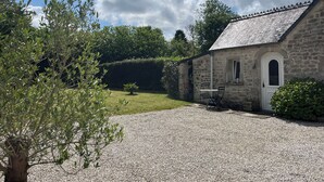 A stone building with a gravel driveway, a small garden, and a tree in the foreground. - Le "33" Gîte de Charme coeur Cotentin (Valognes)