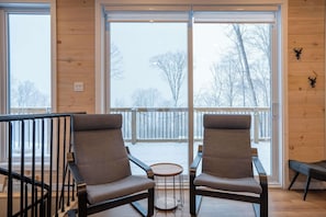 A room with two chairs facing a large window, a small round table, and a wooden floor.
