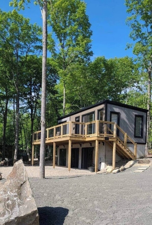 Une cabane moderne dotée d’une terrasse en bois et de nombreuses fenêtres, entourée d’arbres.