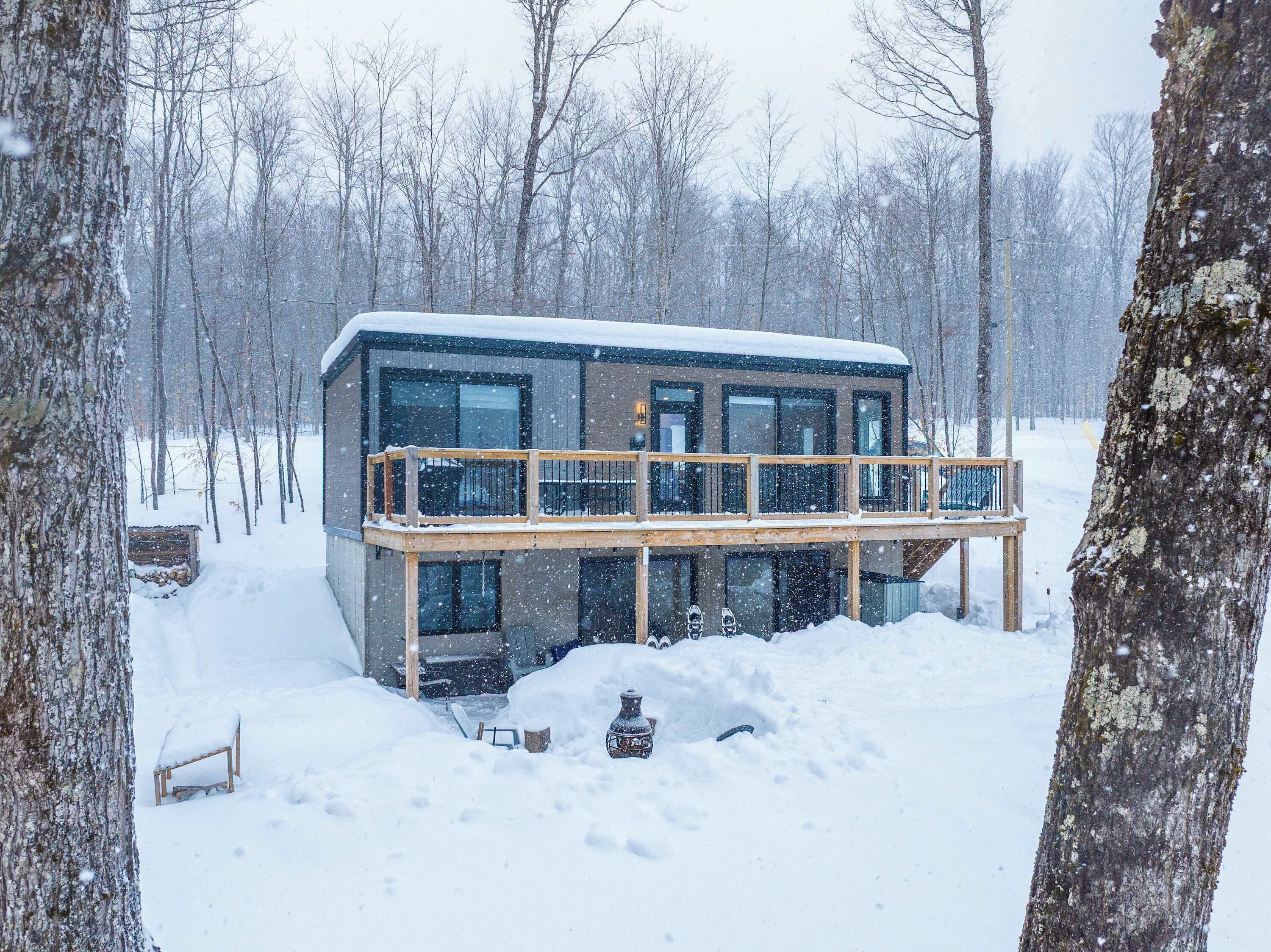 A modern cabin with a balcony, surrounded by snow-covered trees.