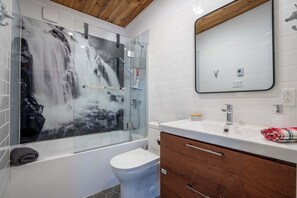 Une salle de bain moderne avec une douche à l’italienne en verre, des toilettes blanches, un meuble-lavabo en bois doté de tiroirs et un grand miroir au-dessus du lavabo.