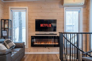 Un salon chaleureux avec une cheminée, un canapé et un téléviseur fixé au mur.
