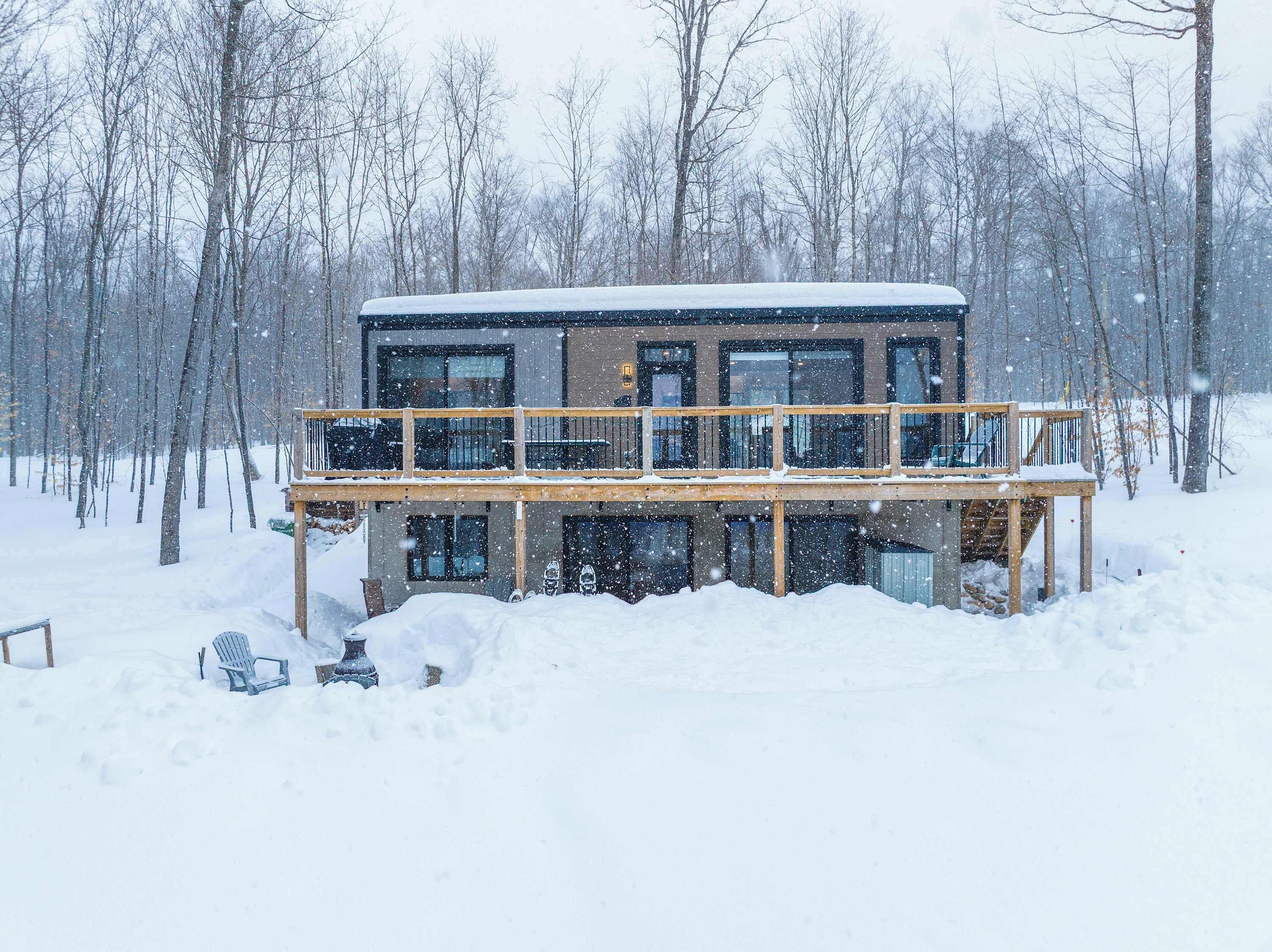 Een moderne cabin met balkon, omgeven door met sneeuw bedekte bomen.