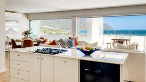 A modern kitchen with a large island, dining area, and a view of the ocean. - Clifton 2bed Penthouse Sea Views Dunmore Horizons (Cape Town)
