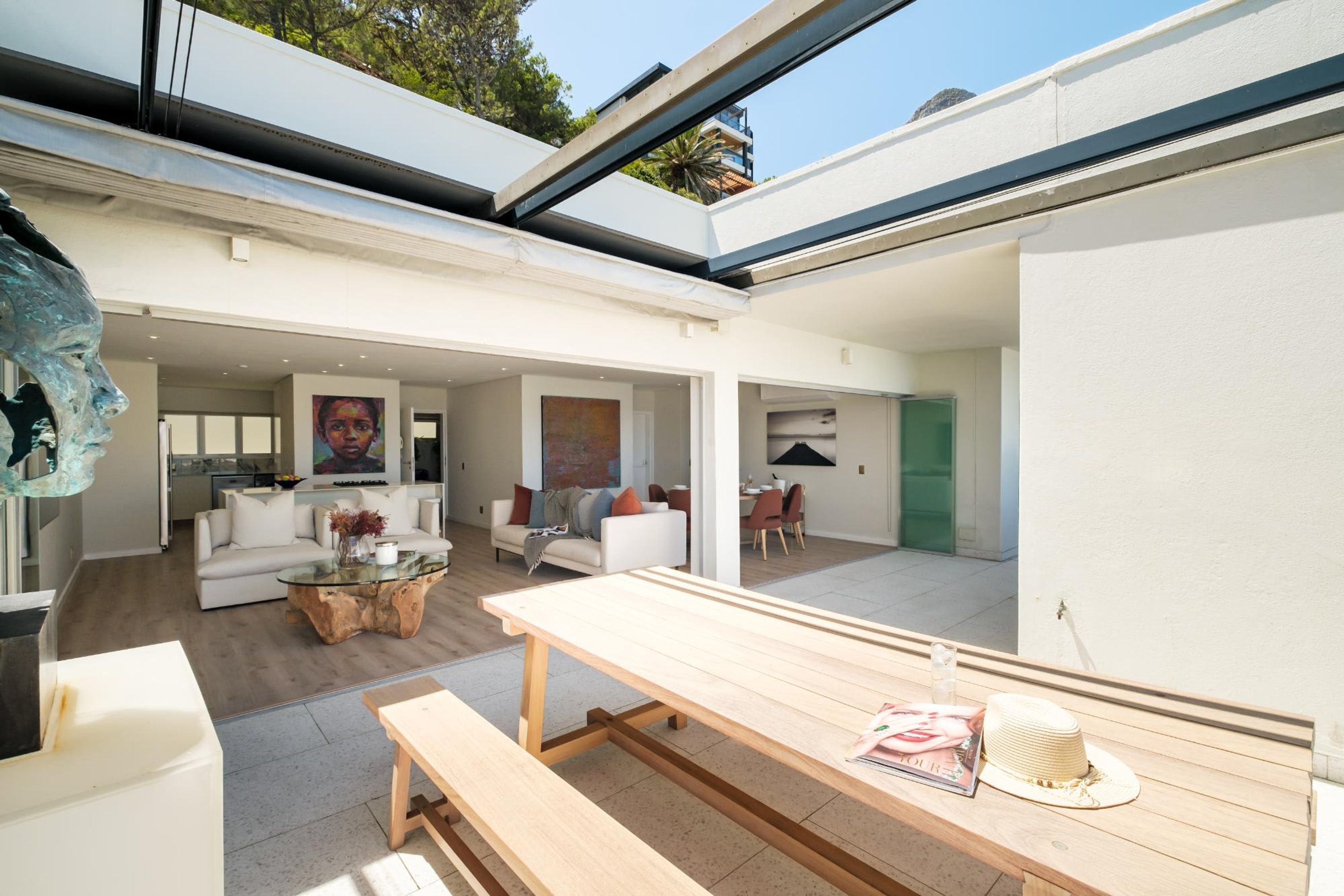 Un intérieur moderne avec un plafond en verre, un banc en bois, un canapé blanc et un coin repas.