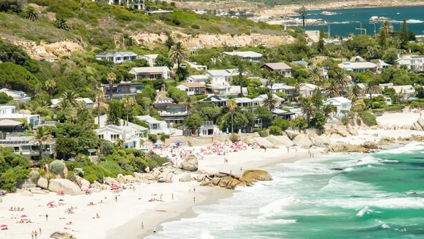A coastal beach with rocky outcrops, a sandy shoreline, and a backdrop of residential buildings. - Clifton 2bed Penthouse Sea Views Dunmore Horizons (Cape Town)
