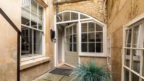 Une petite cour étroite, avec un mur de pierre, une porte blanche et un plant en pot.