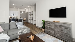 Ett modernt vardagsrum med en grå soffa, ett soffbord i trä och en platt-TV som är monterad på väggen.