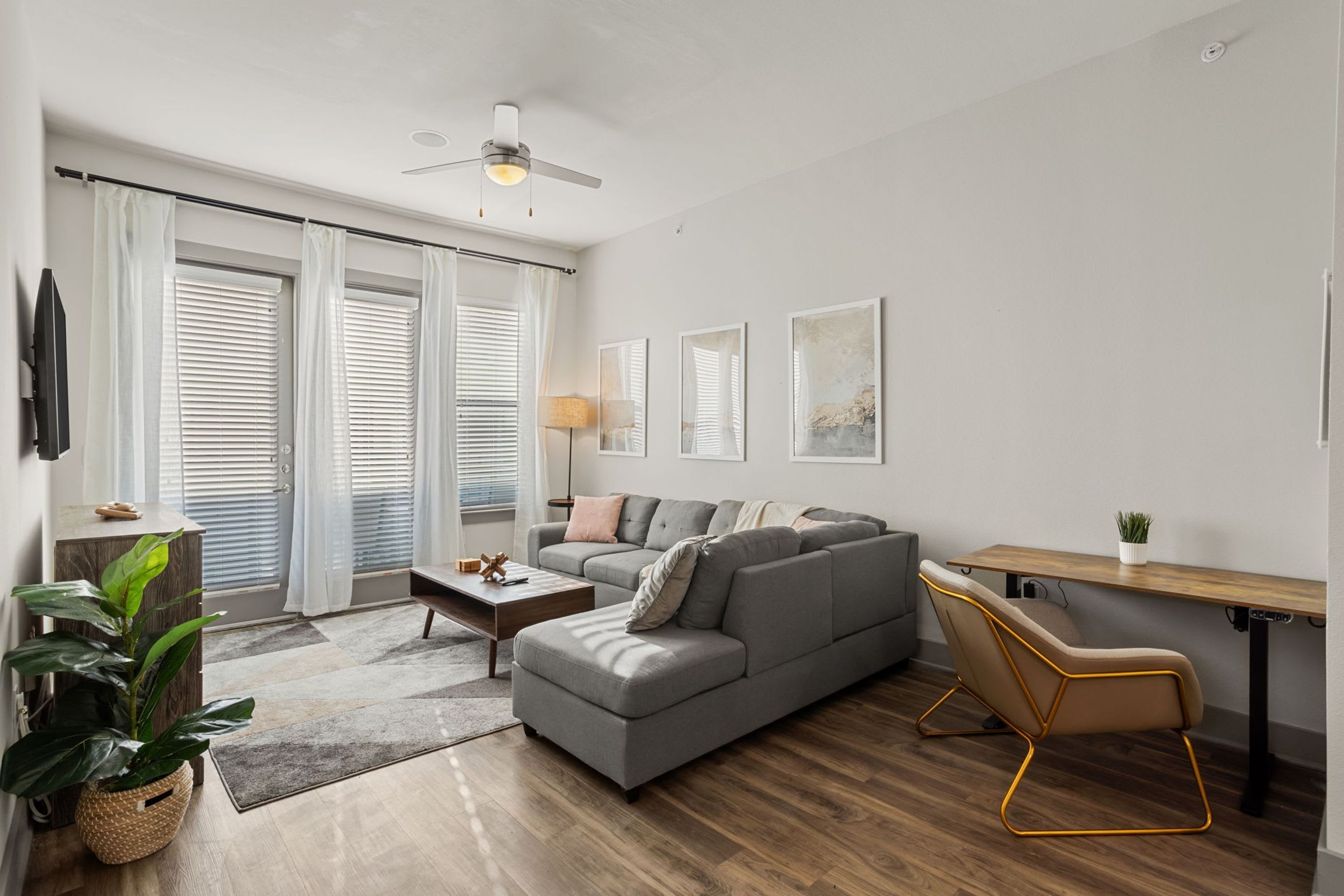 A modern living room with a grey sectional sofa, a wooden coffee table, a floor lamp, and a small desk with a plant.