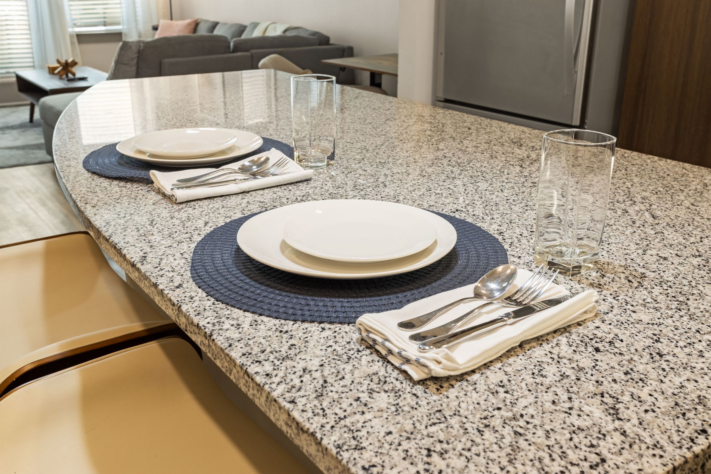Une cuisine moderne dotée de plans de travail en granit, un coin repas avec une table ronde pour quatre personnes et un salon avec un canapé et une table basse.