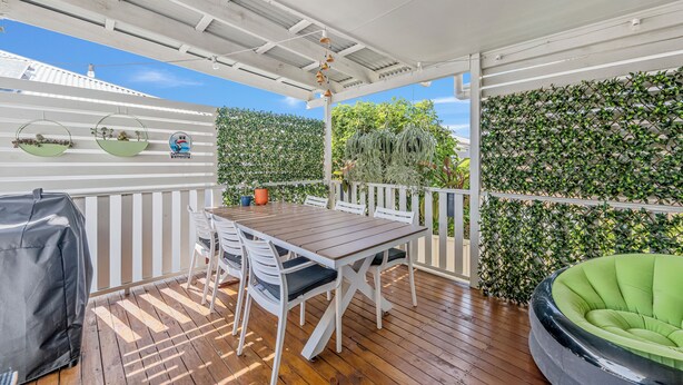 Eine überdachte Terrasse im Freien mit einem Holztisch und -stühlen, einem Grill und einer gepolsterten Sitzecke in Grün.