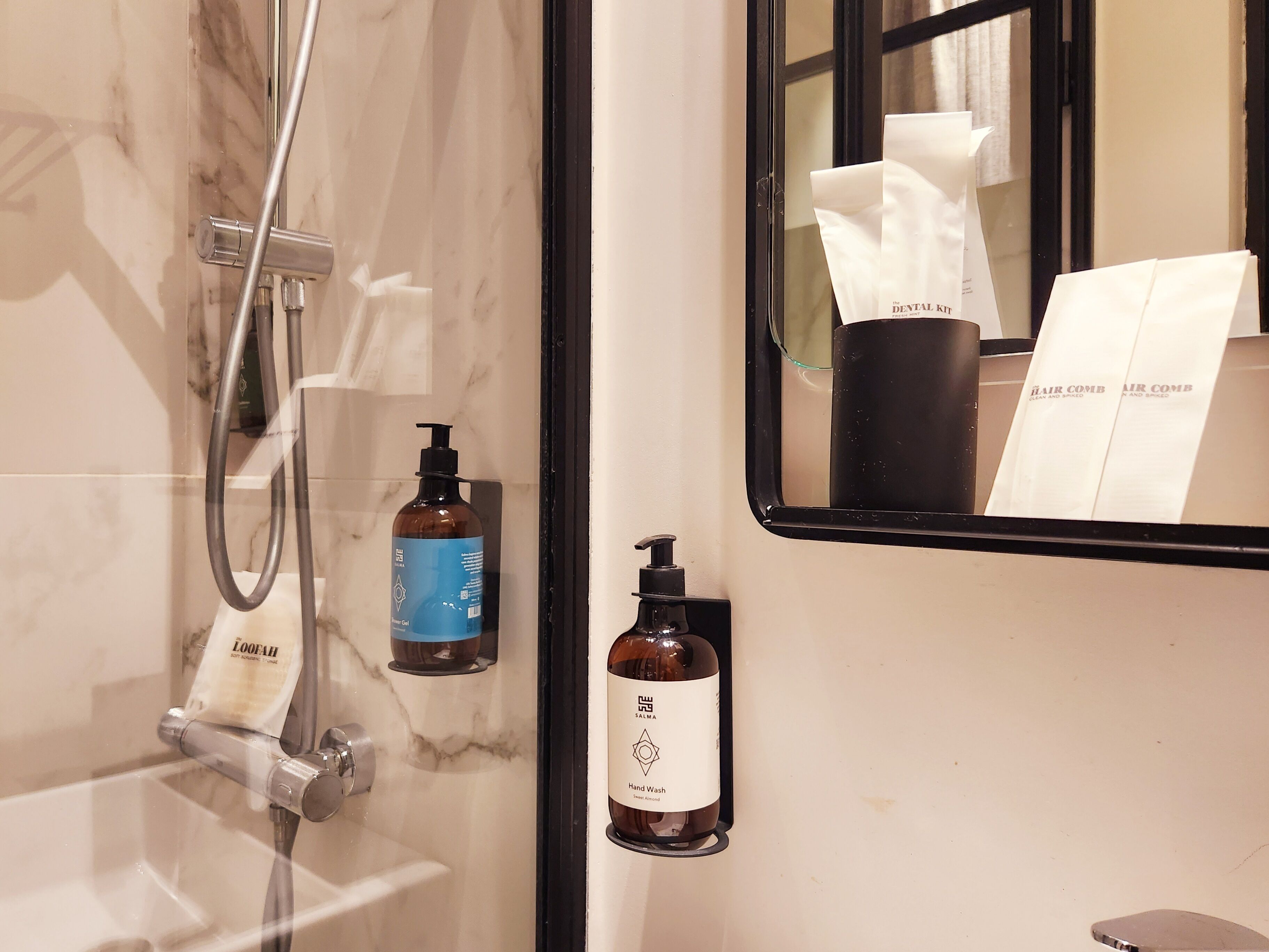 A bathroom with a marble wall, a glass shower enclosure, and toiletries on the wall.