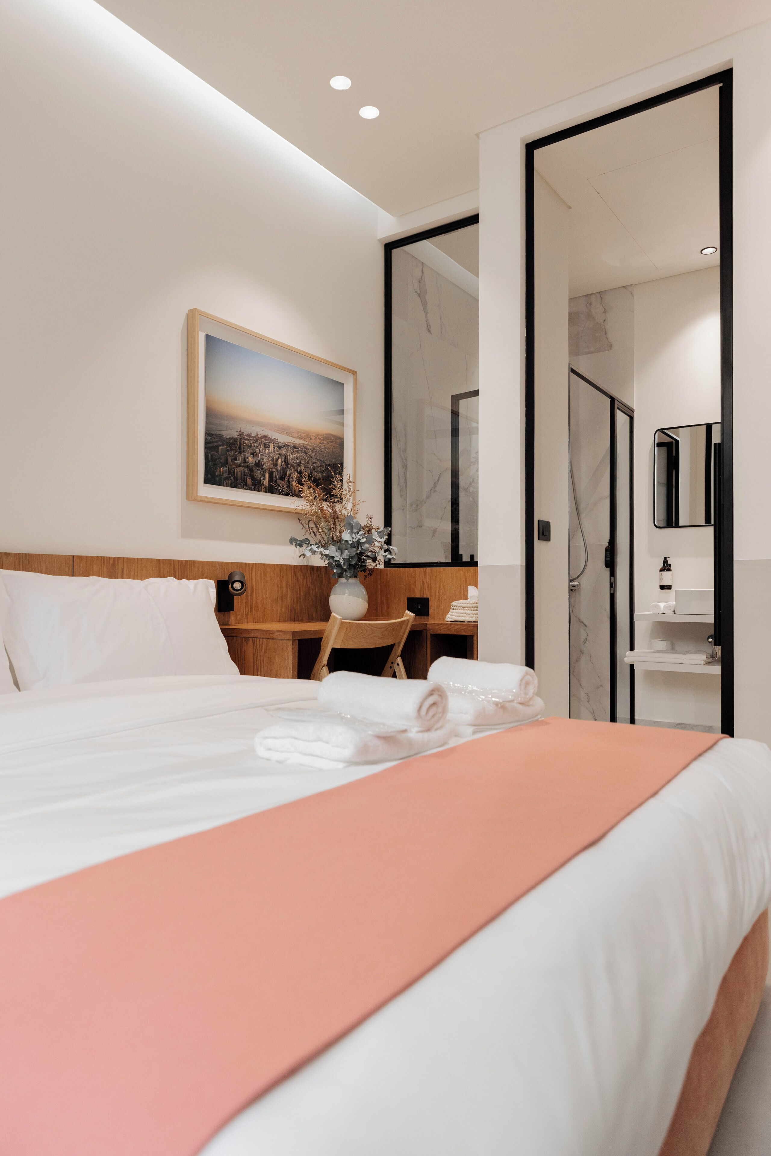 Een hotelkamer met een net opgemaakt bed, een bureau met stoel, een badkamer met spiegel en een schilderij aan de muur.