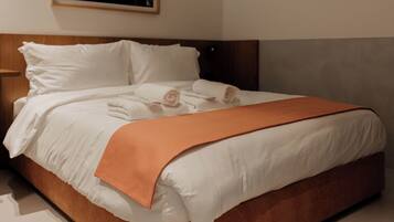 A neatly made bed with white linens and an orange throw blanket, a wooden headboard, and a framed picture on the wall.