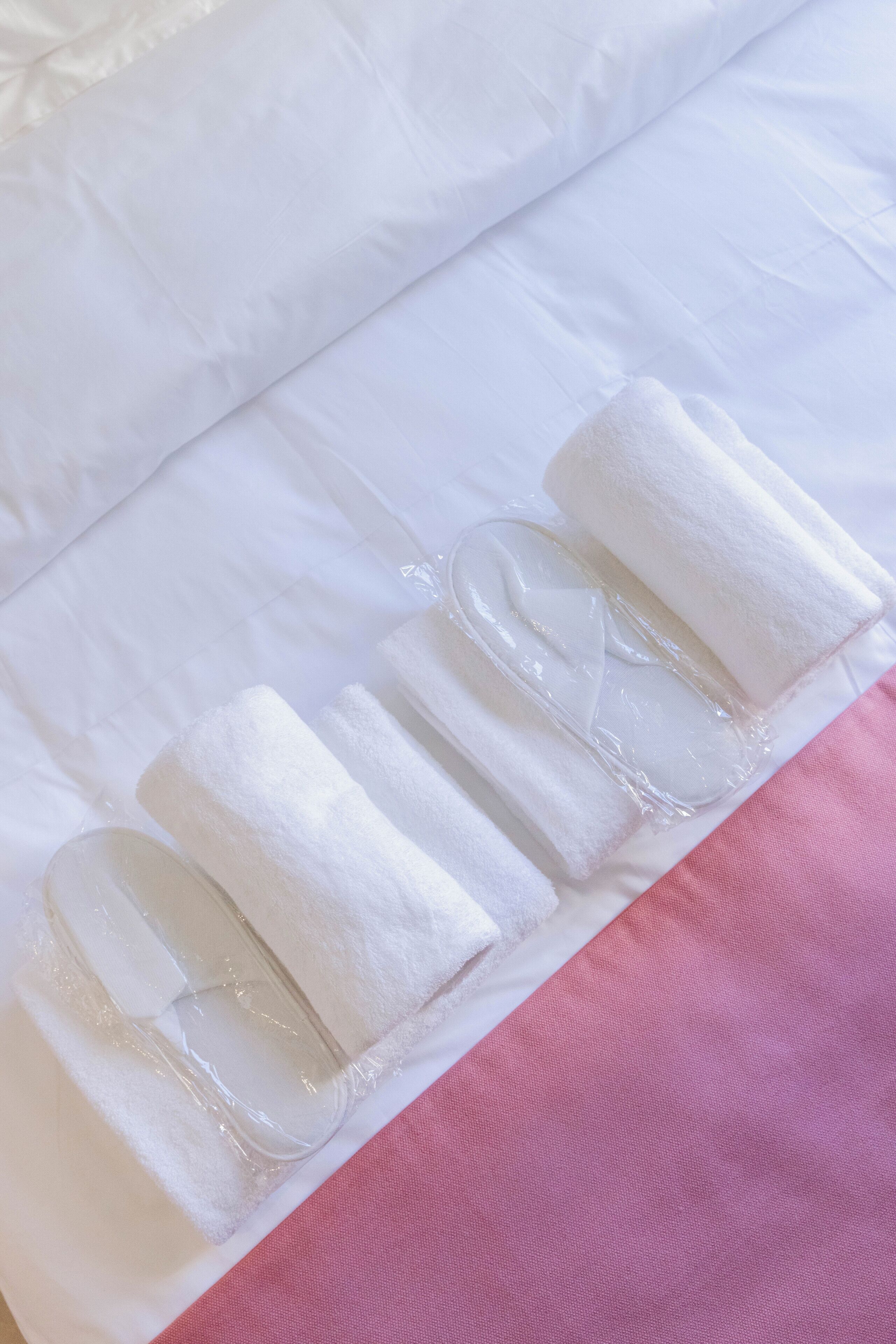 A bed with white bedding and rolled towels.