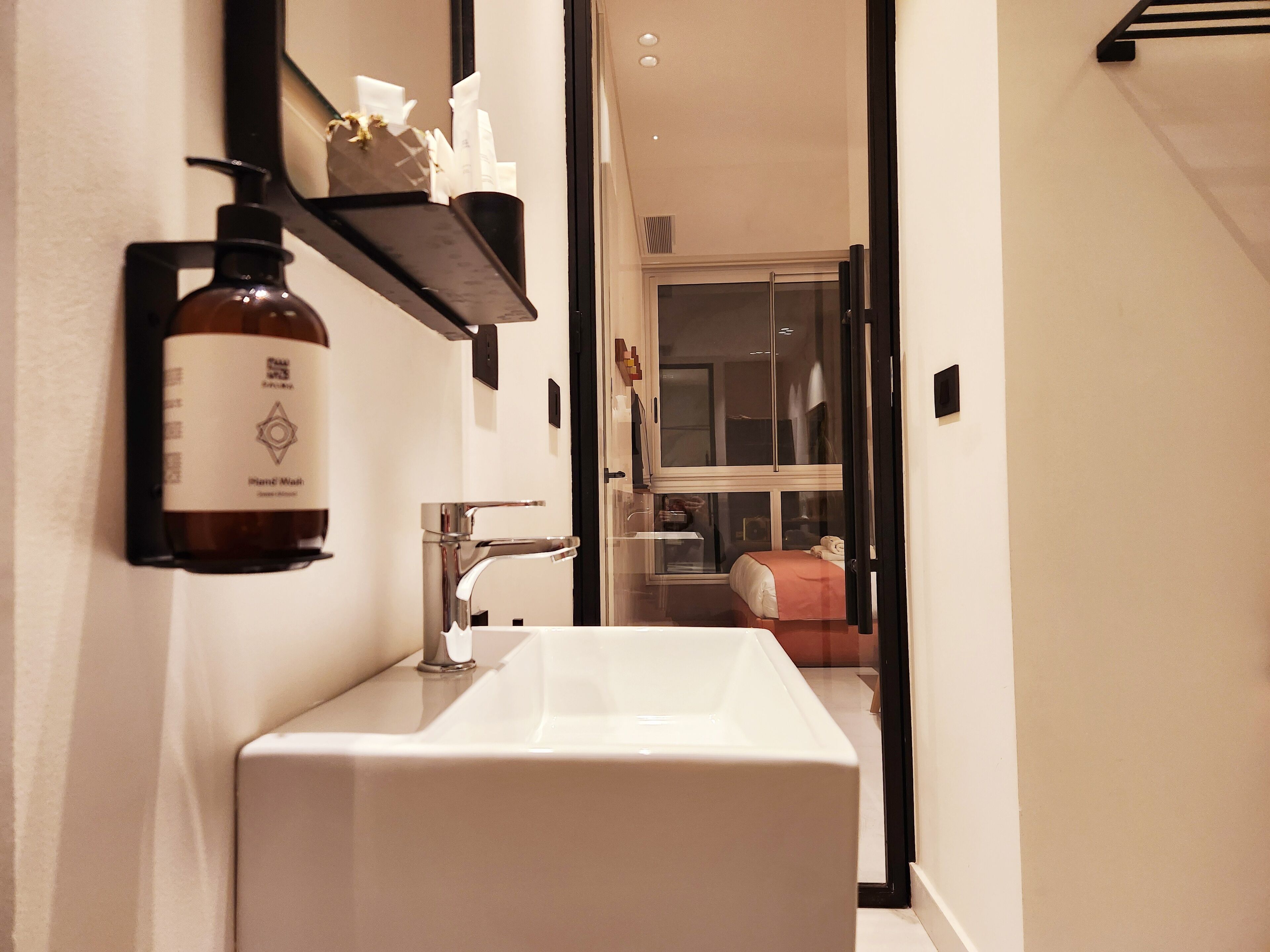 Un baño con un lavamanos blanco, un dispensador de jabón negro y un espejo.