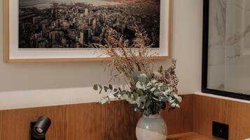 A wooden desk with a vase of dried plants, a framed cityscape picture, and a marble wall.