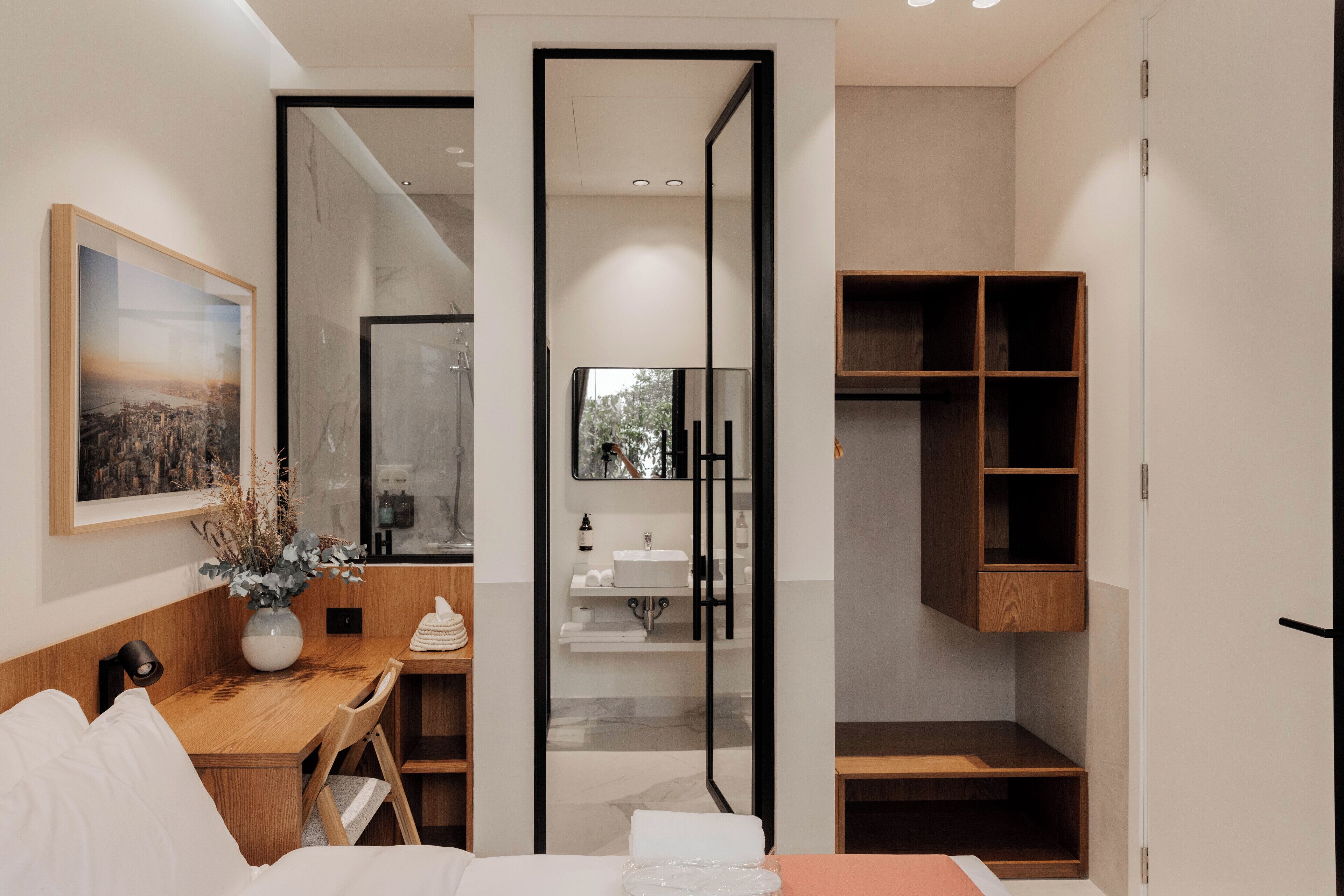 Una habitación de hotel moderna con un escritorio de madera, una cama, un espejo grande y un armario.