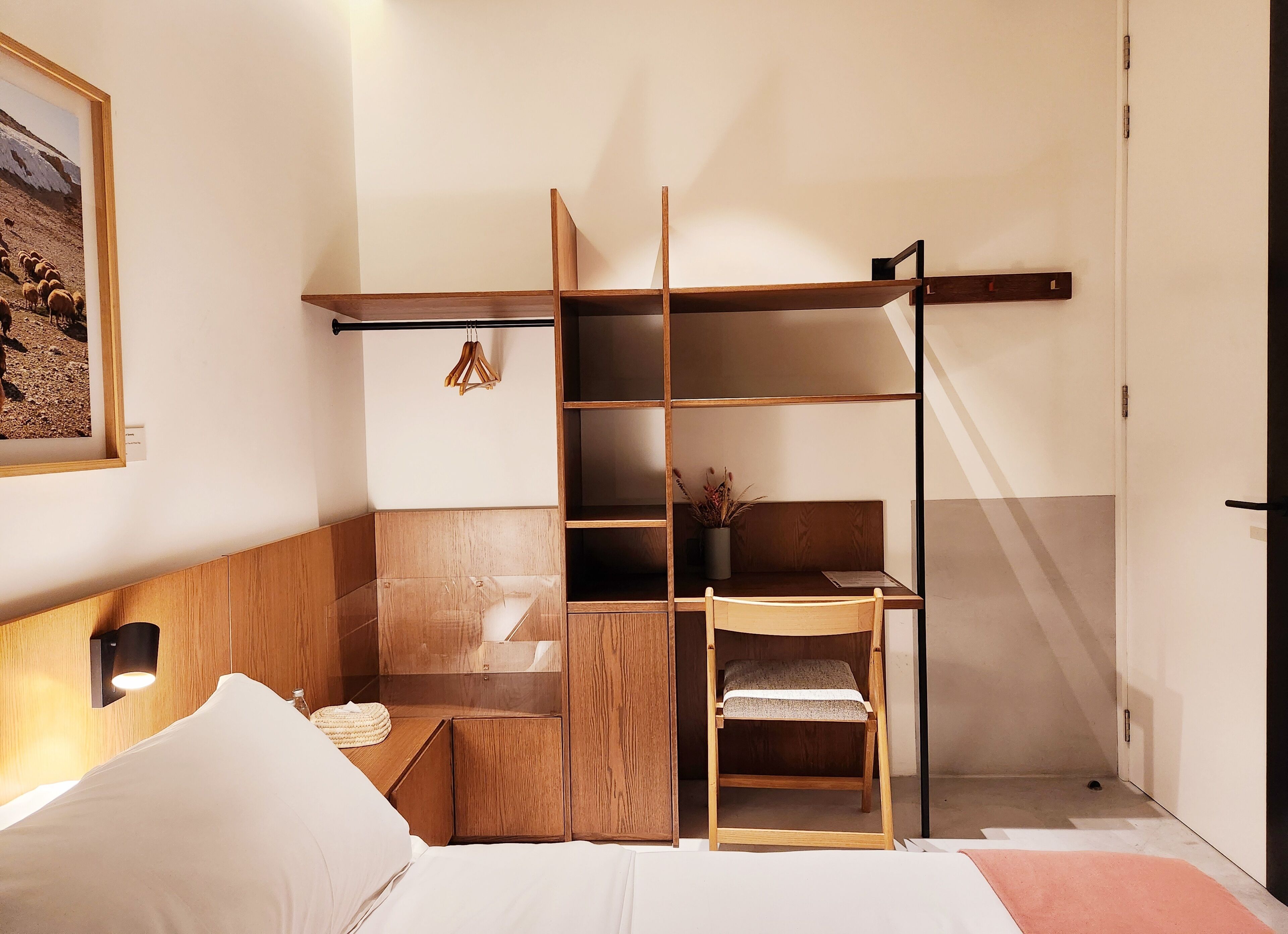 A compact room with a bed, a wooden desk, a chair, and a shelving unit.