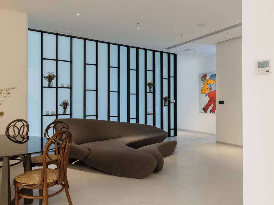 A modern interior with a sectional sofa, a dining table with chairs, and a decorative wall with shelves.
