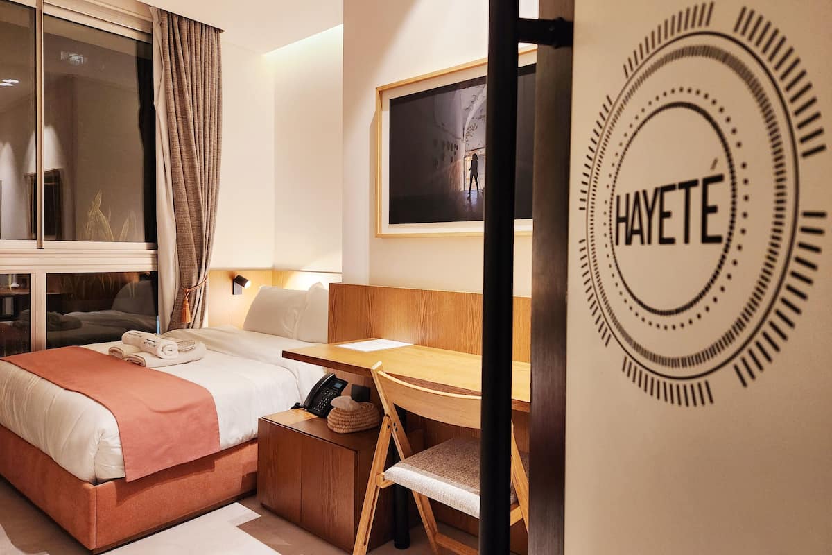Habitación de hotel con cama, escritorio y vistas de la ciudad a través de la ventana.