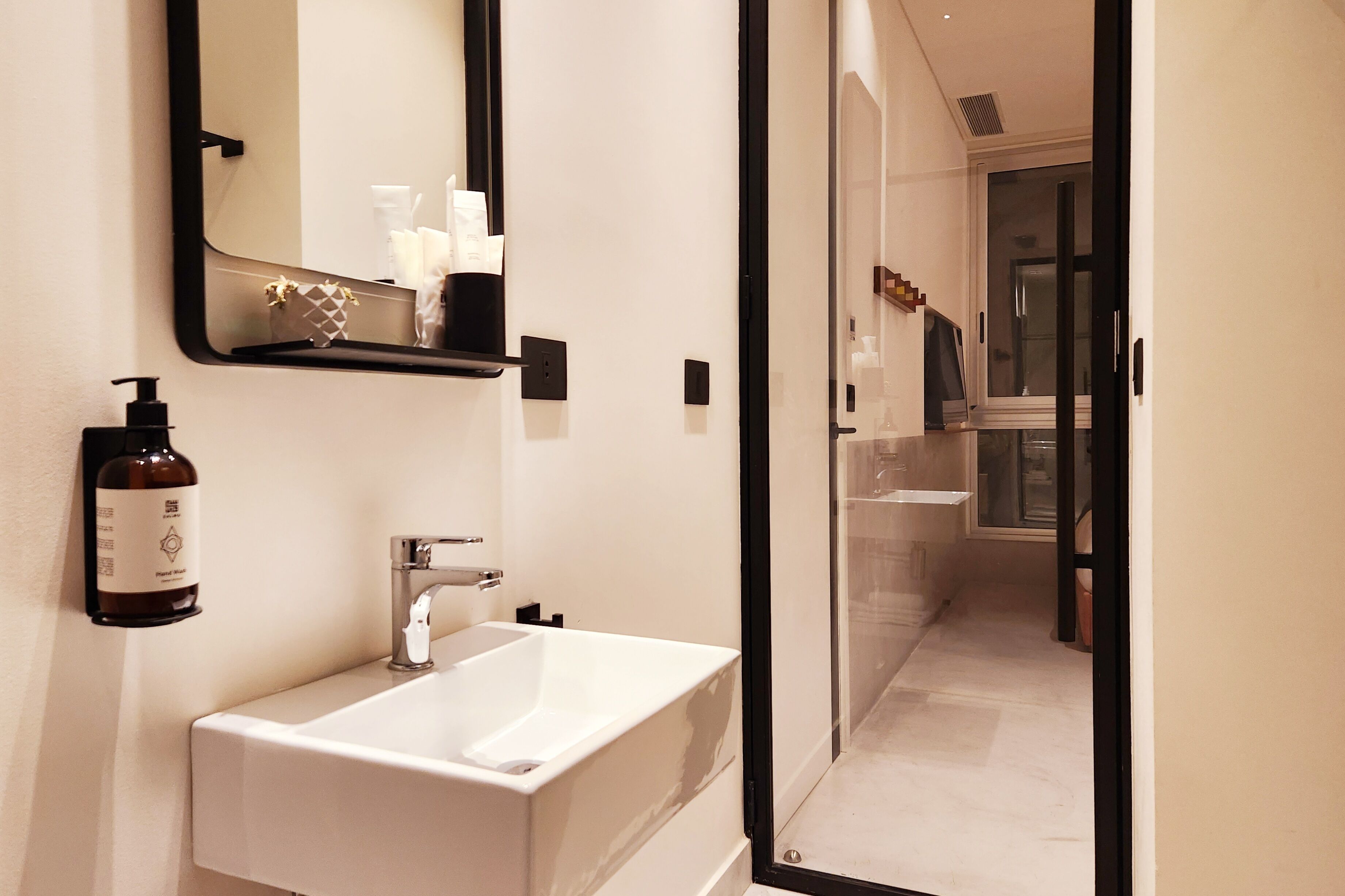 Une salle de bain moderne avec un lavabo blanc, un miroir et un flacon de savon pour les mains.