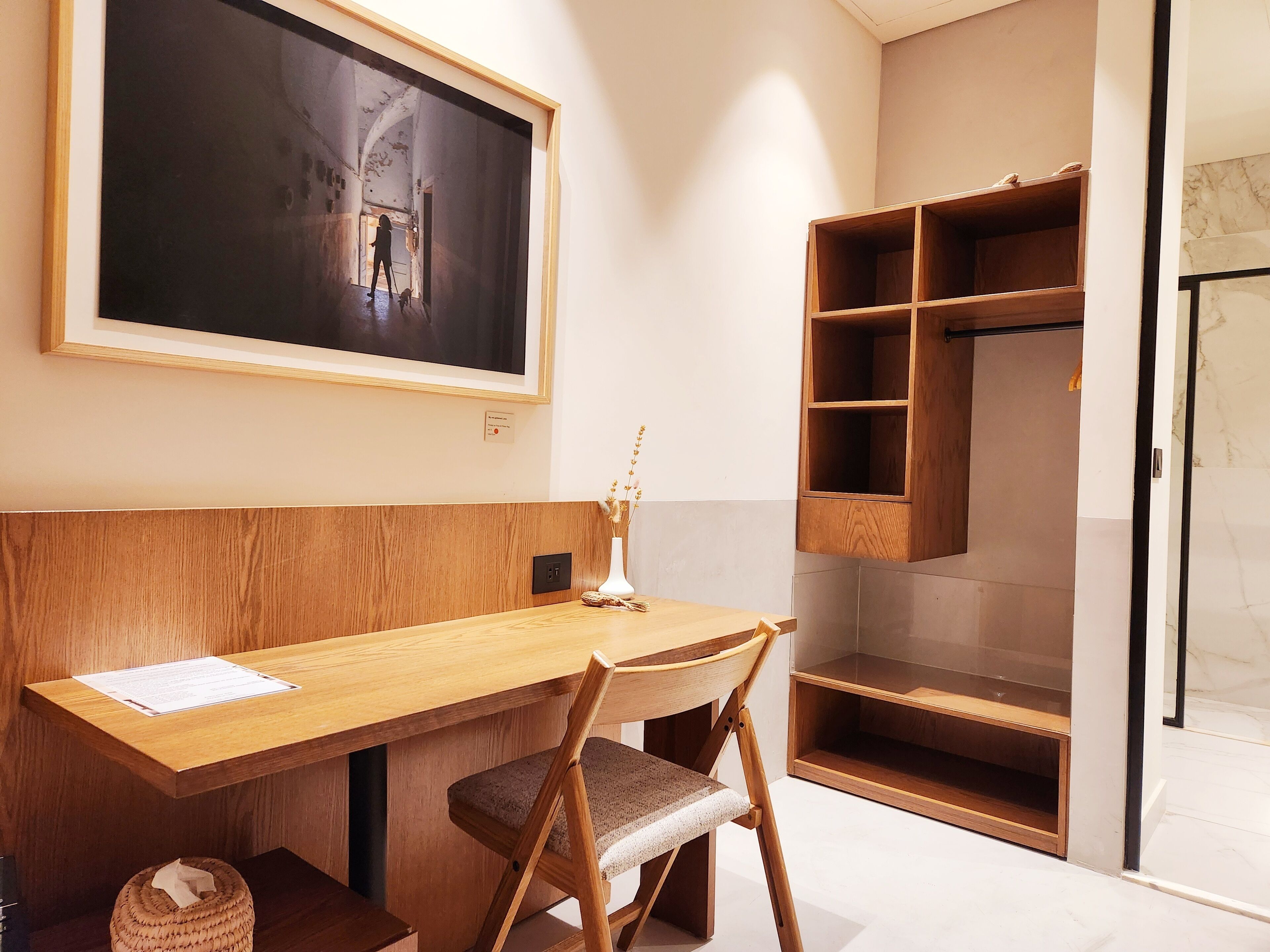 A room with a wooden desk, a chair, a framed picture on the wall, and a wooden shelving unit.