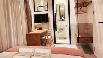 A hotel room with a bed, a desk, a chair, a TV, a mirror, a bathroom, and a wardrobe.