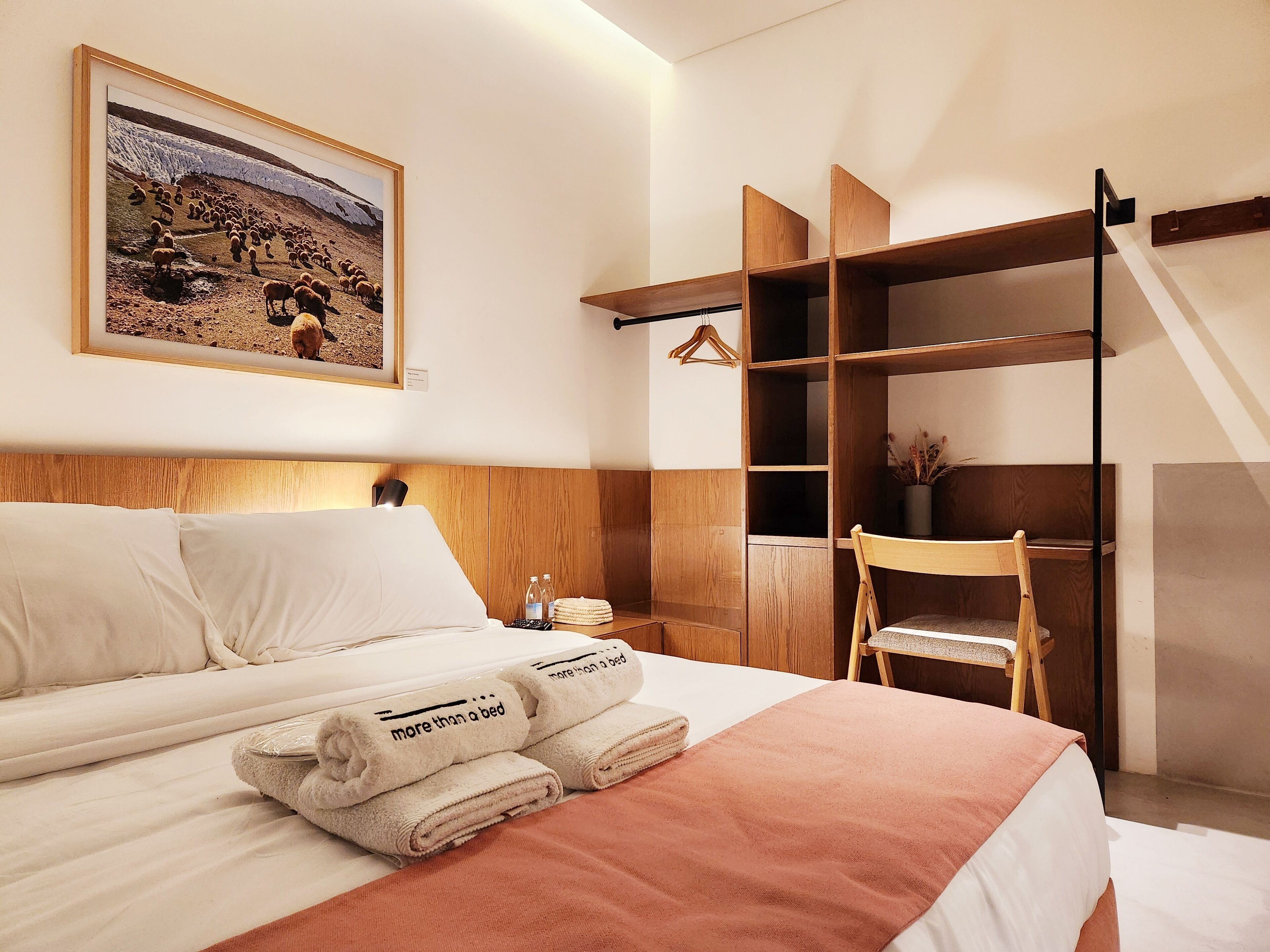 Une chambre d’hôtel avec un lit, une armoire en bois, un tableau au mur et une chaise.
