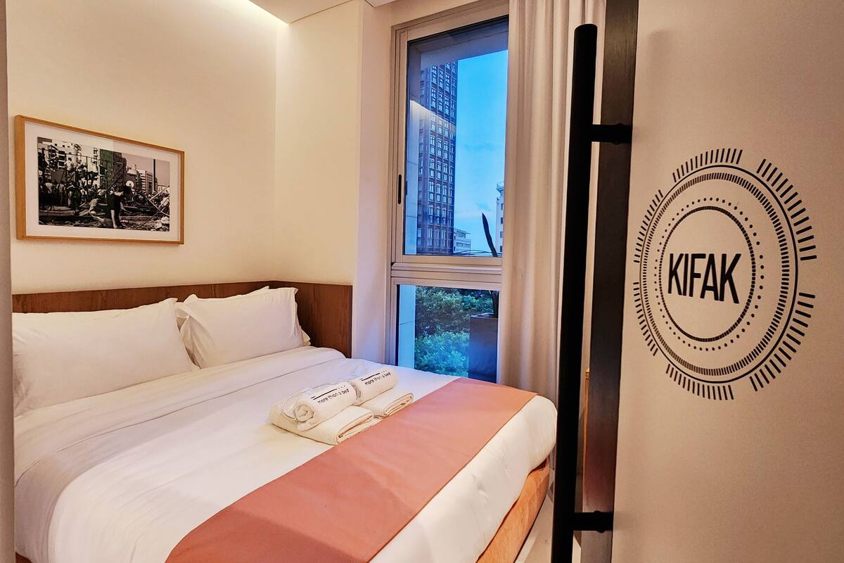 Habitación de hotel con cama, un cuadro en la pared, una ventana con cortinas y un logotipo en la pared.