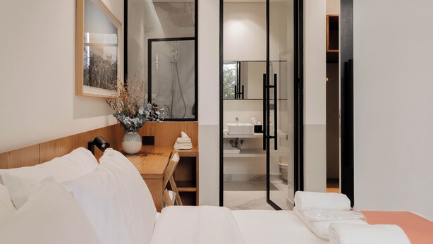 Camera d'albergo moderna con un letto, una scrivania in legno, un bagno con doccia e uno specchio grande.
